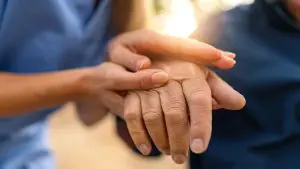 Close-up of an older person's hands, with a healthcare provider gently supporting them, symbolizing care and human connection in aging with autoimmune disease.