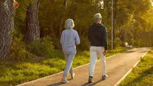 Two people walking side by side on a tree-lined path, suggesting healthy aging and daily activity.